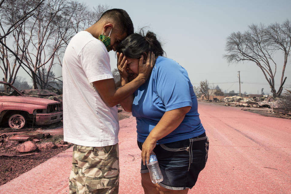 FILE - In this Sept. 10, 2020, file photo, Dora Negrete is consoled by her son Hector Rocha after seeing their destroyed mobile home at the Talent Mobile Estates, in Talent, Ore., after wildfires devastated the region. Two unusual weather phenomena combined to create some of the most destructive wildfires the West Coast states have seen in modern times. (AP Photo/Paula Bronstein, File)