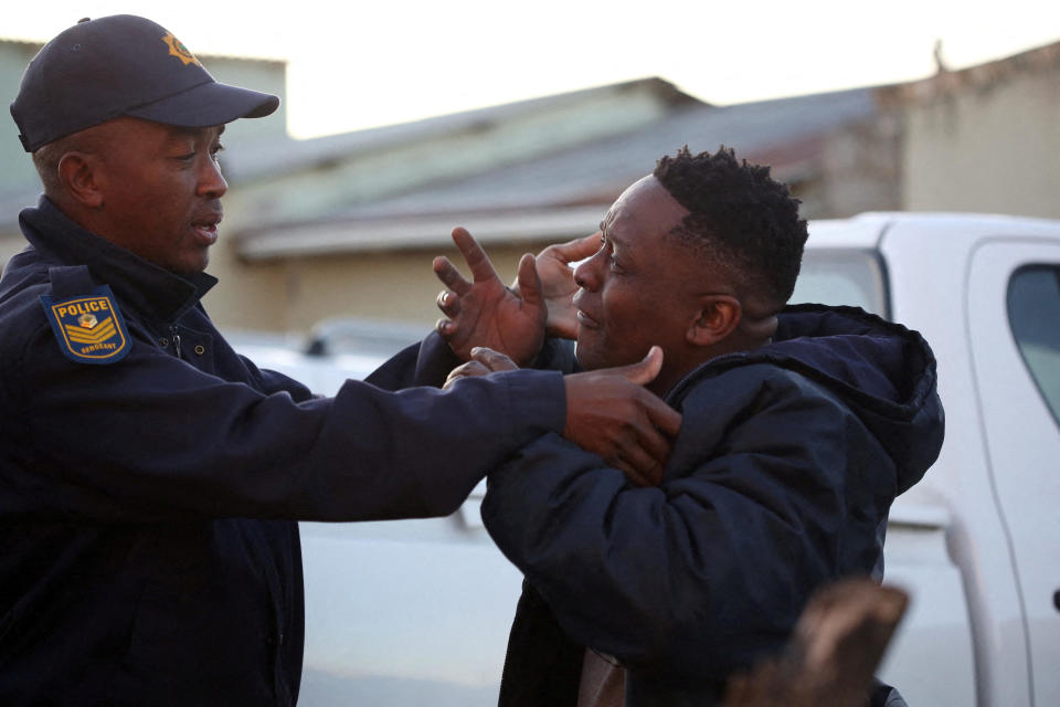 A family member reacts next to a police officer as forensic personnel investigate the deaths of patrons found inside the Enyobeni Tavern, in East London, South Africa, June 26, 2022. / Credit: Reuters/Stringer