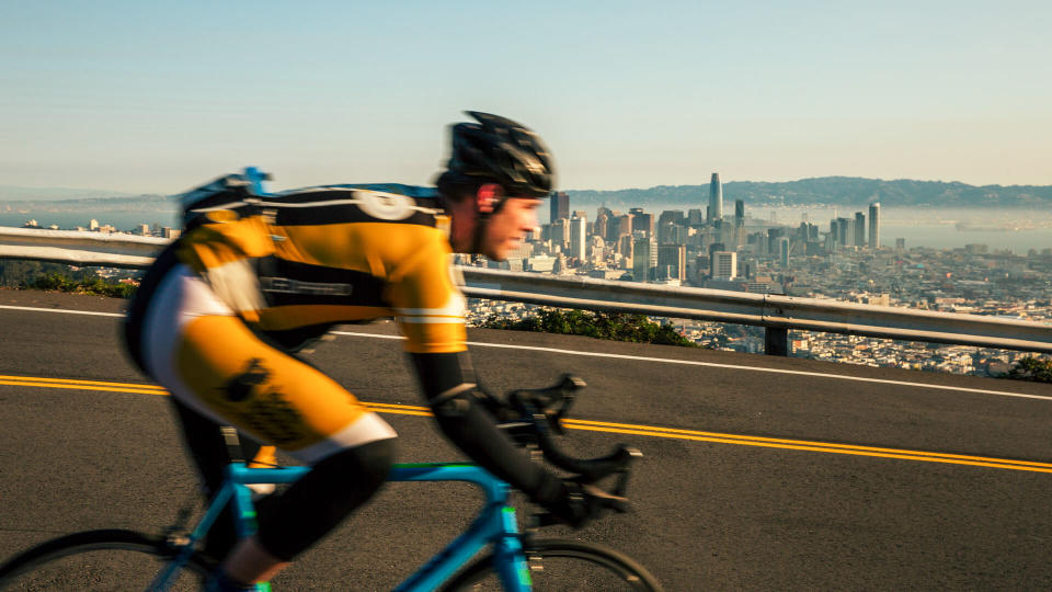 Man bicycling on Twin Peaks in San Francisco with downtown in background.