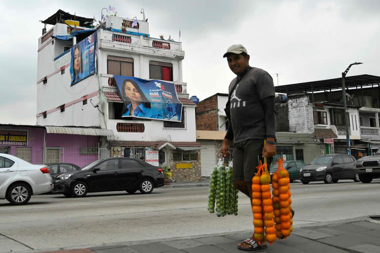 Un vendedor de frutas camino en una calle de Guayaquil, delante de carteles proselitistas de Luisa González. (Rodrigo BUENDIA / AFP)