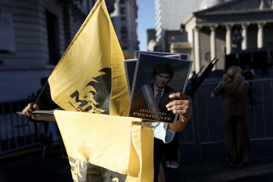 A supporter of Argentina's newly sworn-in President Javier Milei holds pictures of him outside the government house in Buenos Aires, Argentina, Sunday, Dec. 10, 2023. (AP Photo/Rodrigo Abd)