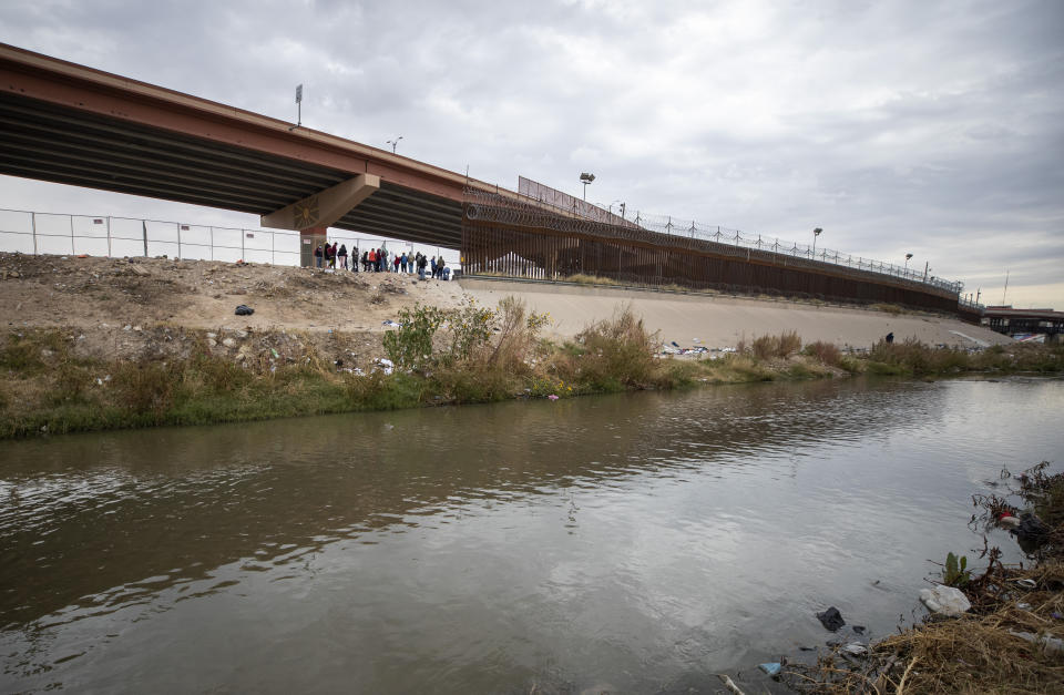 A small group of migrants wait for the Border Patrol at the border fence in El Paso, Texas, after crossing the Rio Grande from Ciudad Juarez, Mexico, Sunday, Dec. 18, 2022. Texas border cities were preparing Sunday for a surge of as many as 5,000 new migrants a day across the U.S.-Mexico border as pandemic-era immigration restrictions expire this week, setting in motion plans for providing emergency housing, food and other essentials. (AP Photo/Andres Leighton)