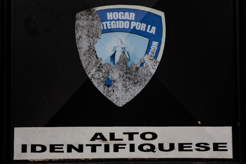 In this March 15, 2017 photo, stickers, one with an image of the Virgin Mary with a partial text that reads in Spanish "Home protected by" and another sign that reads "Stop, identify yourself," are stuck on the entrance to Virgen de la Asuncion Safe Home, in San Jose Pinula, Guatemala. On March 7, about 60 girls escaped from the shelter by jumping from the roof of the facility to the wall, and from there into the trees. (AP Photo/Moises Castillo)