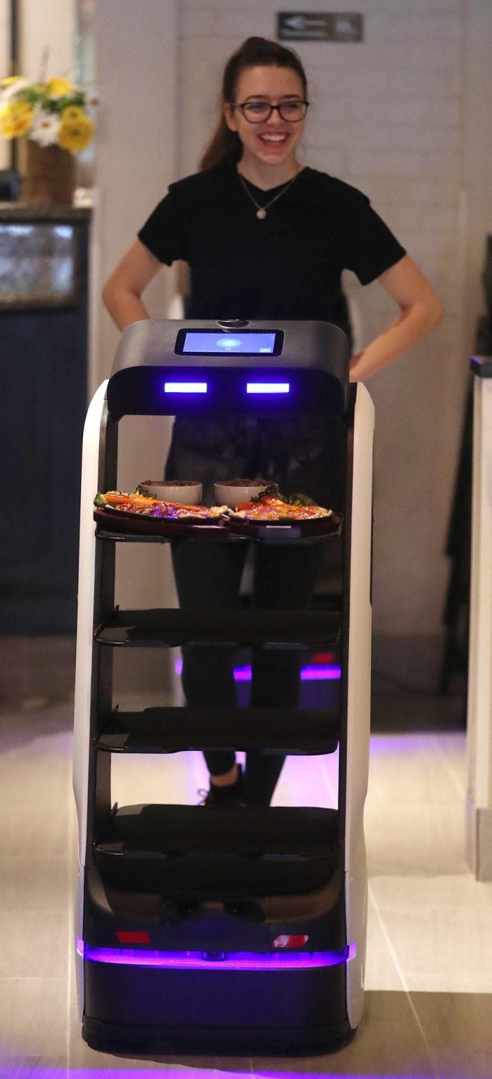 Katie Cox, a server at Sake Japanese Fusion, follows a robot to a table. The robot is a high-tech food runner that assists the human server at the new restaurant at Summit Mall in Fairlawn.