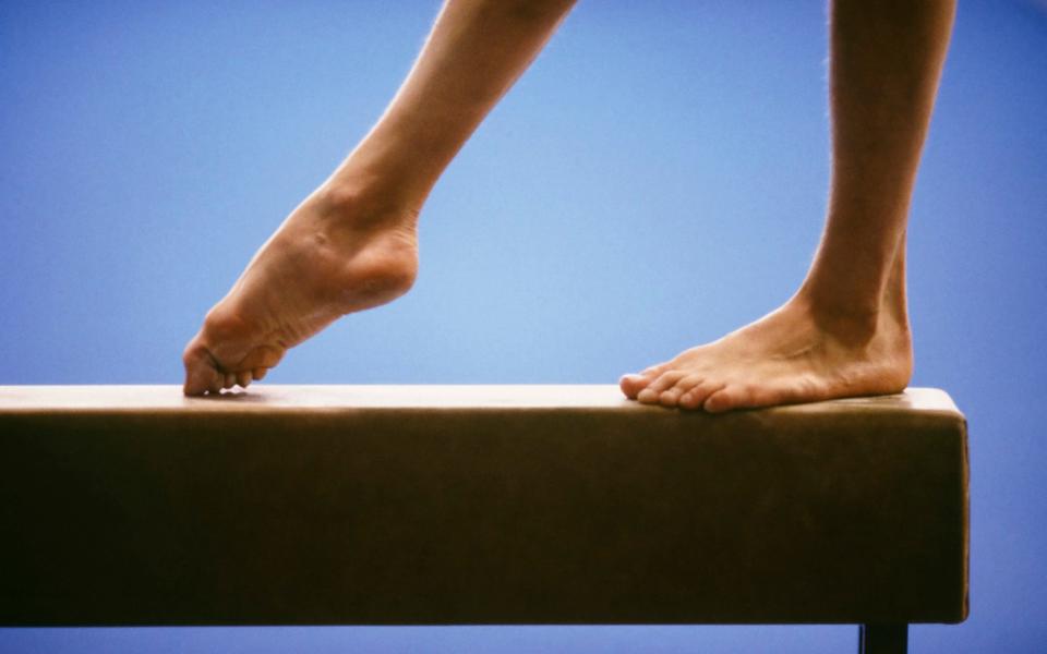 Female gymnast performing on balance beam - David Mason