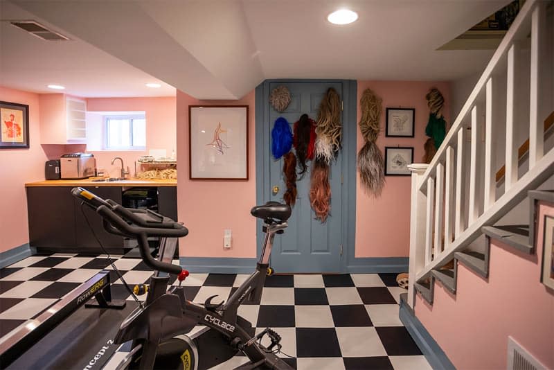 Various wigs on wall in pink and blue basement.