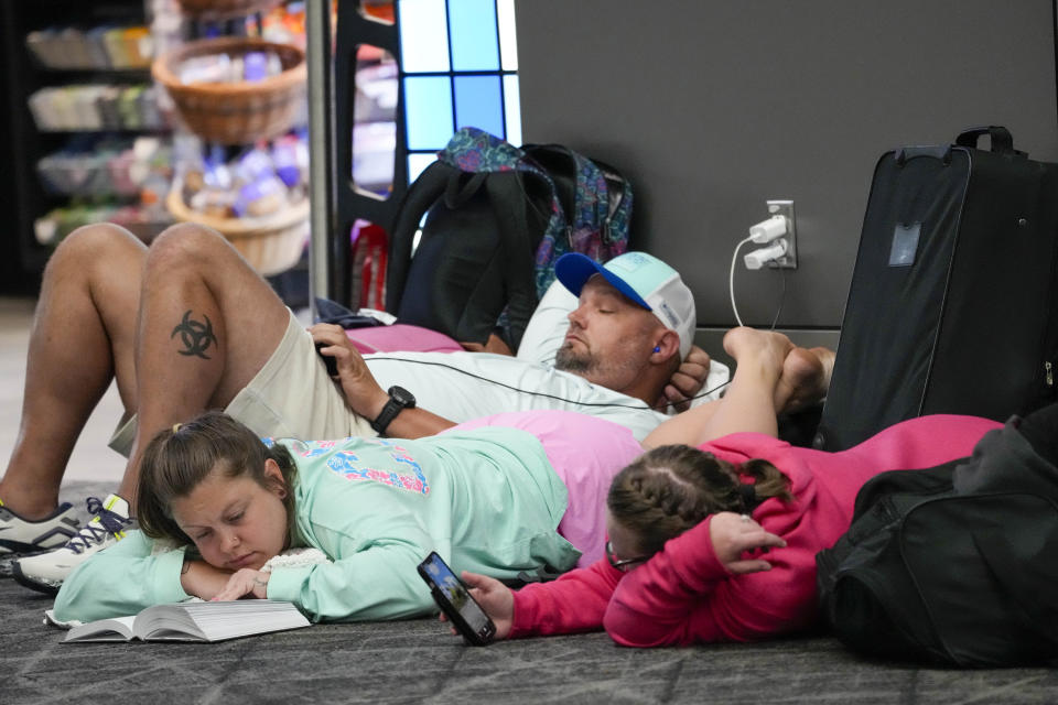 Travelers use their electronic devices while lying on the floor of the departures area of Terminal B at LaGuardia Airport, Tuesday, June 27, 2023, in New York. Travelers waited out widespread delays at U.S. airports on Tuesday, an ominous sign heading into the long July 4 holiday weekend, which is shaping up as the biggest test yet for airlines that are struggling to keep up with surging numbers of passengers. (AP Photo/Mary Altaffer)