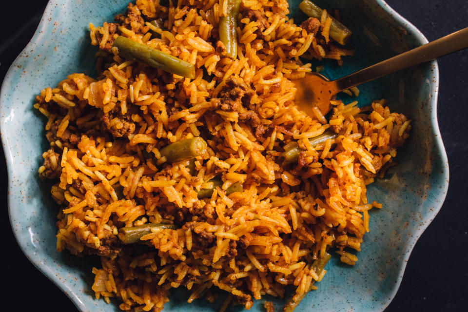 A plate of seasoned rice mixed with ground meat and green beans, with a fork resting on the side of the bowl