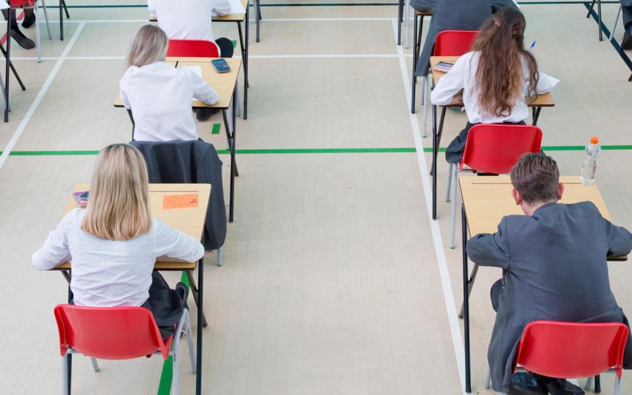 Teachers supervising private students taking examination at desks - Getty Images