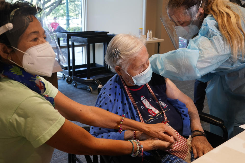 Patricia Wasseman, holds Hermina Levin's hands as nurse Eva Diaz administers the Pfizer vaccine at John Knox Village, Wednesday, Dec. 16, 2020, in Pompano Beach, Fla. Nursing home residents and health care workers in Florida began receiving the Pfizer vaccine this week. (AP Photo/Marta Lavandier)