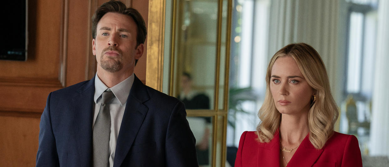  Chris Evans and Emily Blunt standing together in a very nice looking room in Pain Hustlers. 