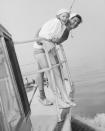 <p>Lucille Ball and Desi Arnaz lean over the railing of a motorboat, while sporting skipper hats and bathing suits. Ball wears an oversized white button-down as a cover-up. </p>