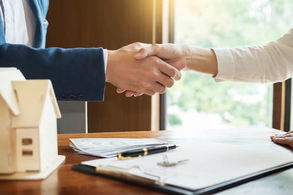 A man and a woman shaking hands over a desk.