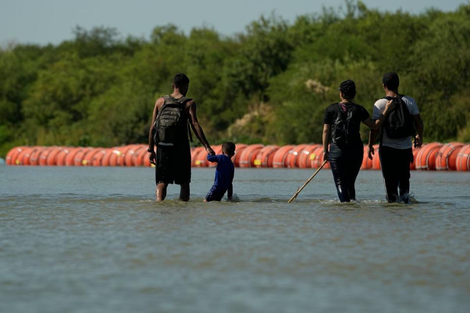 Migrants crossing into the US from Mexico walk along large buoys being used as a floating border barrier on the Rio Grande in Eagle Pass, Texas (Copyright 2023 The Associated Press. All rights reserved)