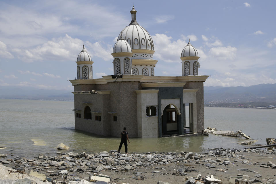 In this Friday, Oct. 5, 2018, file photo, a man stands at a mosque surrounded by water from the massive earthquake and tsunami in Palu, Central Sulawesi, Indonesia. (AP Photo/Aaron Favila, File)