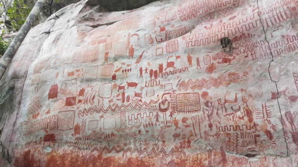  A massive rock wall covered in red-colored rock art. 