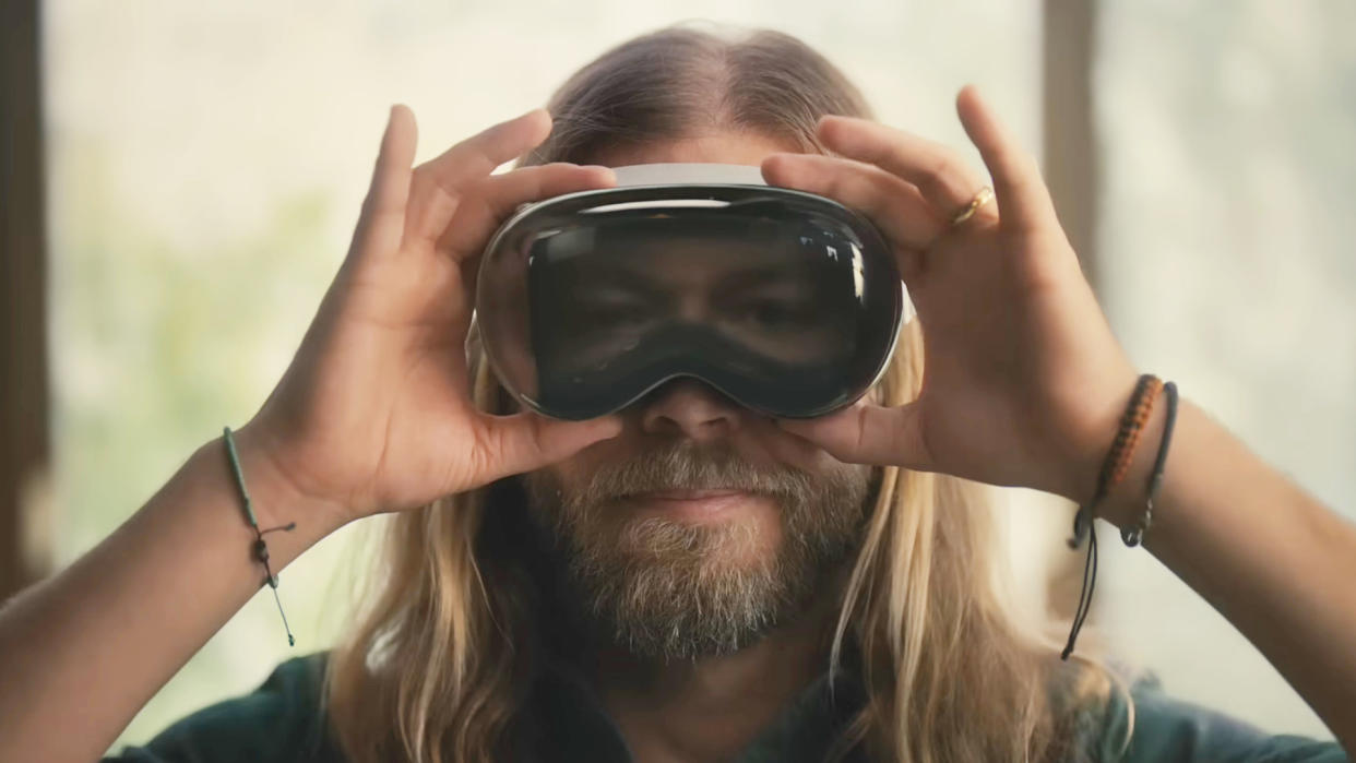  A screenshot from the advert for the Apple Vision Pro, showing a man holding on to one like goggles. 