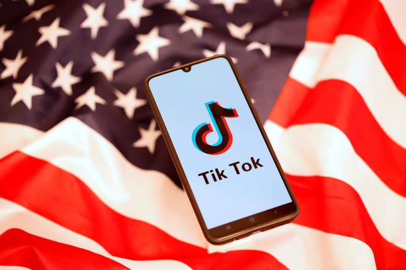 El logotipo de TikTok en la pantalla de un teléfono móvil sobre el fondo de una bandera estadounidense