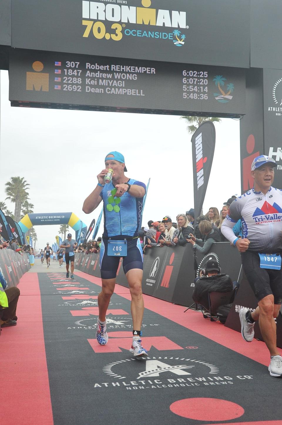 Bobby Rehkemper crosses finish line at IRONMAN in Oceanside, California chugging a beer.