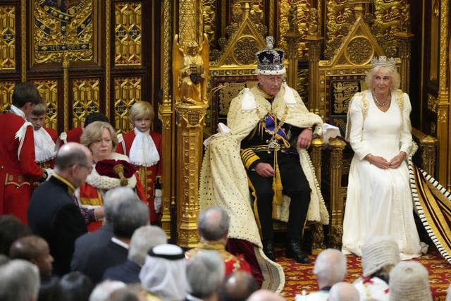 The King sat in his throne next to the Queen after his Robe of State was adjusted by his pages 