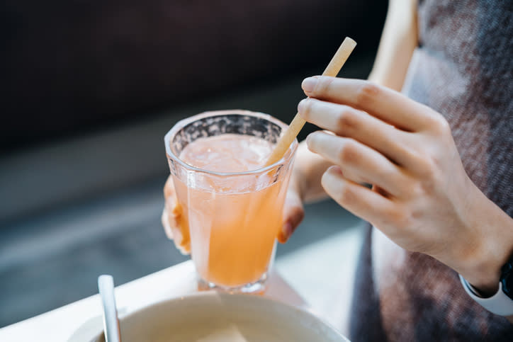 Close-up of a person's hands holding a glass of juice with a straw