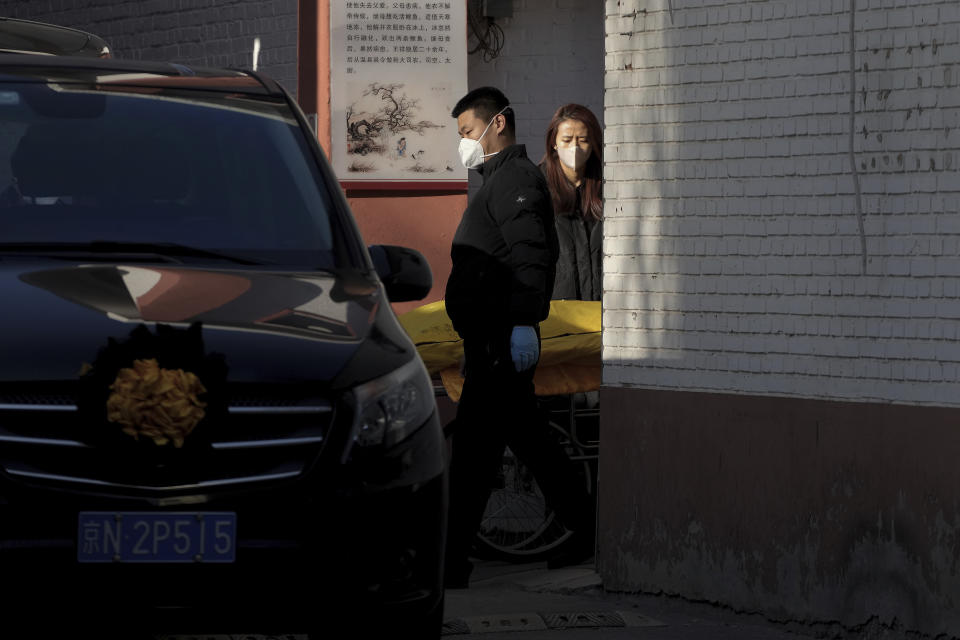 A woman watches the transfer of a deceased body wrapped in yellow to a vehicle parked next to a fever clinic in Beijing, Monday, Dec. 19, 2022. Chinese health authorities on Monday announced two additional COVID-19 deaths, both in the capital Beijing, that were the first reported in weeks and come during an expected surge of illnesses after the nation eased its strict "zero-COVID" approach. (AP Photo/Andy Wong)