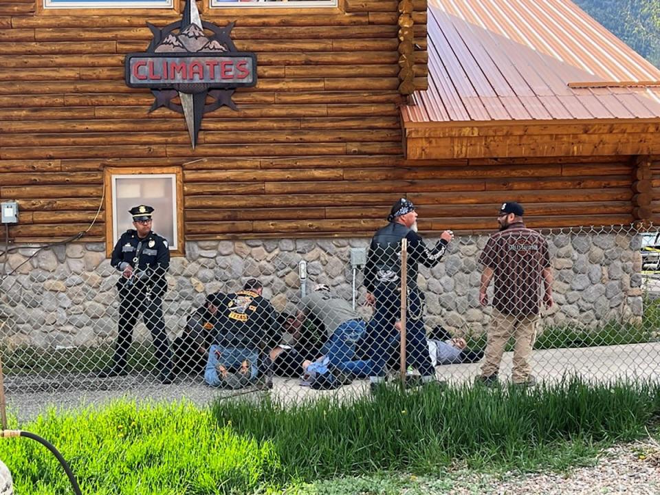 Un agente de policía monta guardia mientras un hombre con un parche de Bandidos MC brinda asistencia a un motociclista herido en Red River, Nuevo México, tras un tiroteo entre miembros de dos bandas de motociclistas en el rally anual de motos del Día de los Caídos (VÍA REUTERS)