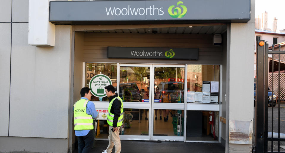 Photo shows front of Woolworths store with two people in high-vis out front. 
