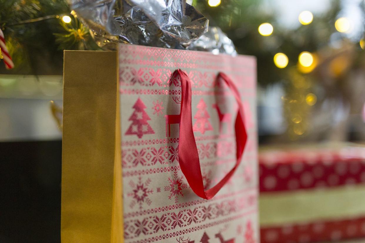brown gift bag with red ribbon handle and red christmas tree and snowflake print on the bag