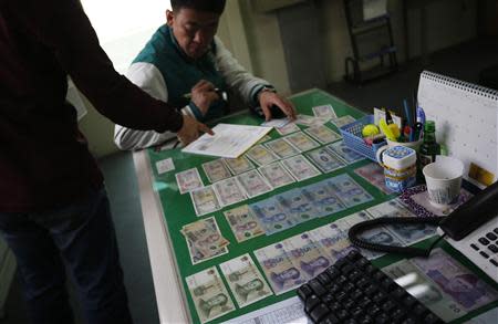 A Chinese applicant fills in application forms for South Korean driver's licenses as Chinese Yuan are seen among the banknotes of various countries banknotes on a desk at a driving school in Siheung March 27, 2014. REUTERS/Kim Hong-Ji