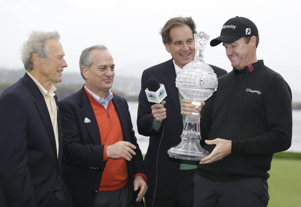 Jimmy Walker, right, looks over his trophy after it was presented to him by actor and director Clint Eastwood, left, on the 18th green of the Pebble Beach Golf Links after winning the AT&T Pebble Beach Pro-Am golf tournament Sunday, Feb. 9, 2014, in Pebble Beach, Calif. AT&T CEO Andy Geisse, second from left, and broadcaster Jim Nantz, second from right, look on. (AP Photo/Eric Risberg)