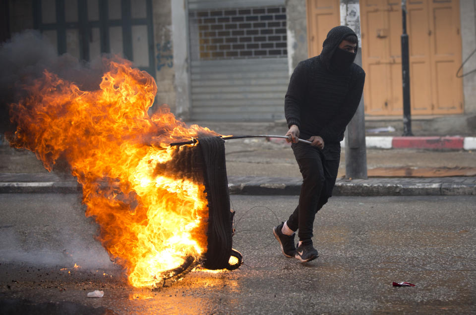 A Palestinian demonstrator burns tires during a protest over an Israeli plan to build a new Jewish neighborhood in the heart of the region's largest city, Monday, Dec. 9, 2019, in the West Bank city of Hebron. (AP Photo/Majdi Mohammed)