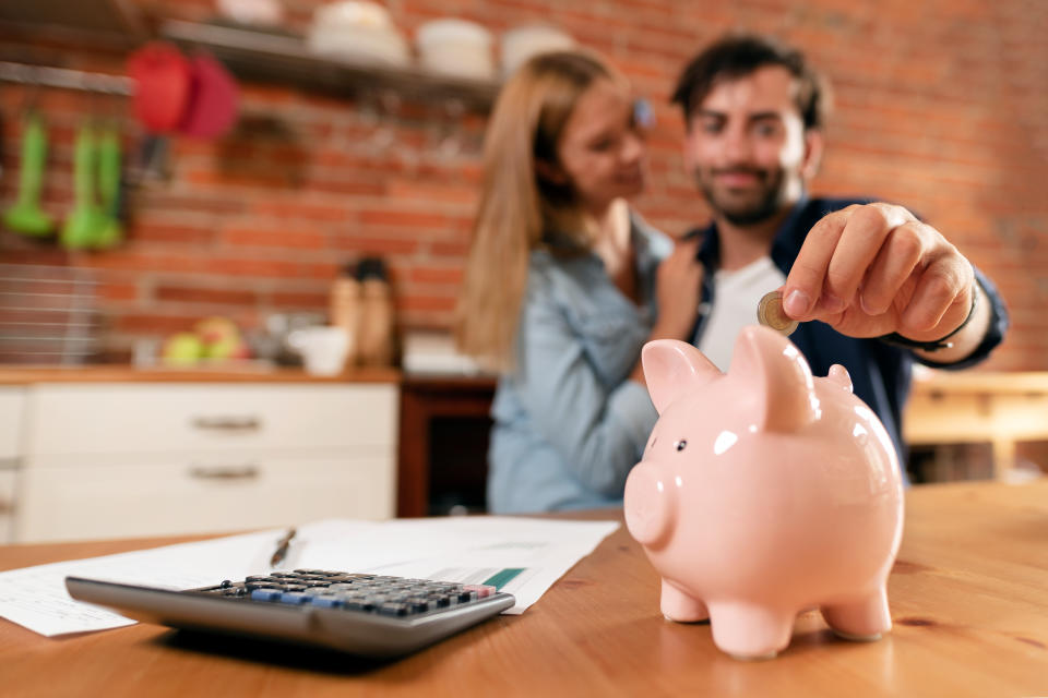 Happy couple inserting coin in piggybank. Home budget, family finance concept. Wide photo with space for your text