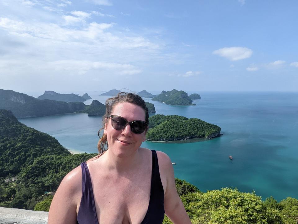 A woman posing for a picture in front of a turquoise sea with green islands.