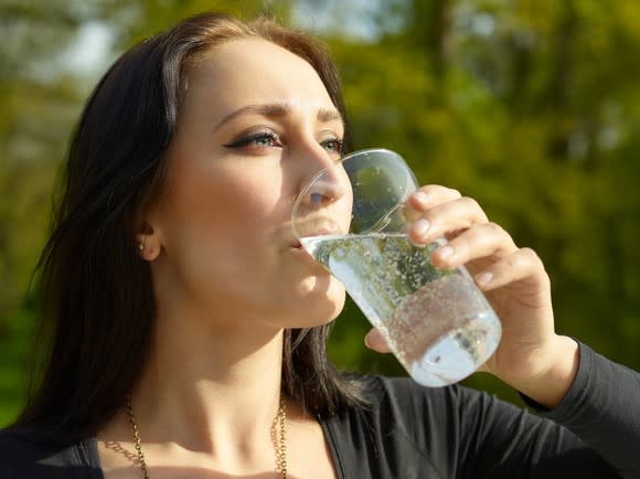 A woman drinks sparkling water from a glass.