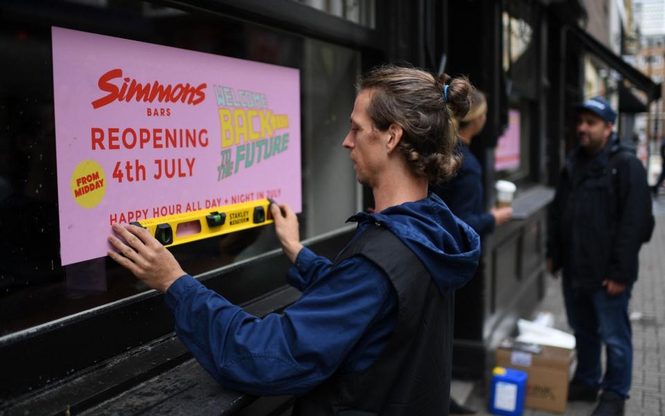 A man works to affix a sign advertising the planned July 4 re-opening of a bar in Soho - DANIEL LEAL-OLIVAS/AFP