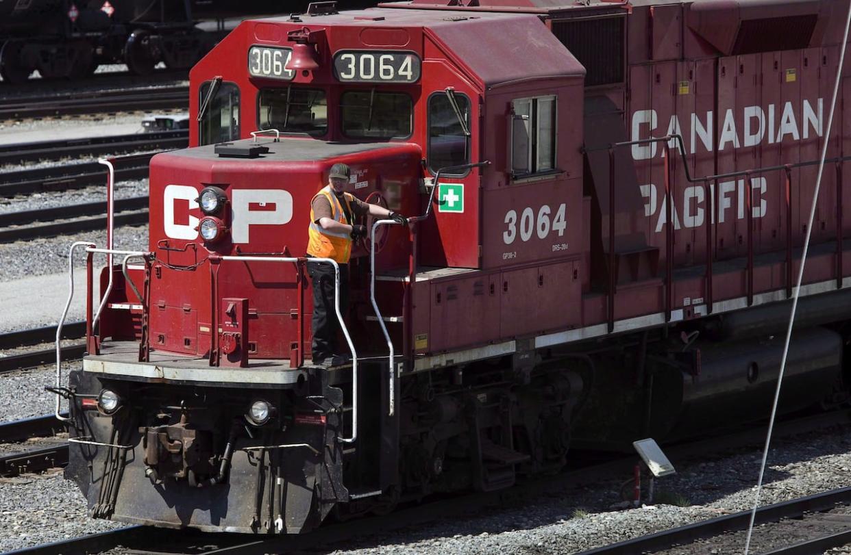 A Canadian Pacific Railway employee walks along the side of a locomotive in a marshalling yard in Calgary in 2012. A train derailed and two people were hospitalized after a crash east of Revelstoke on Friday. (Jeff McIntosh/The Canadian Press - image credit)