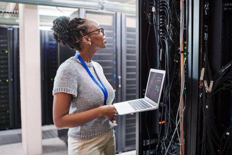 A person looks at the server hardware while holding a laptop.