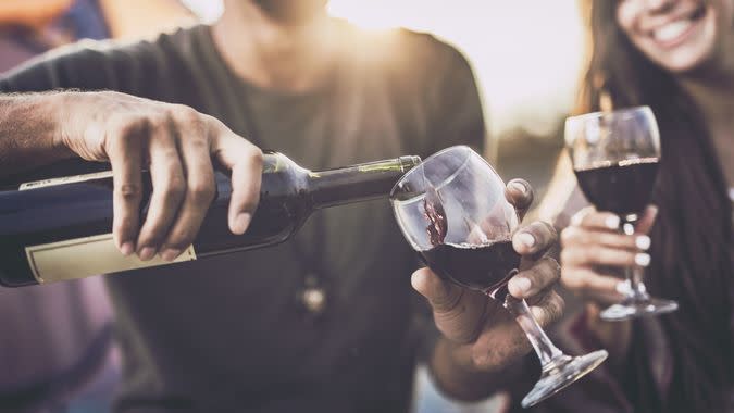 Close up of a couple drinking wine outdoors while man is pouring it into a glass.