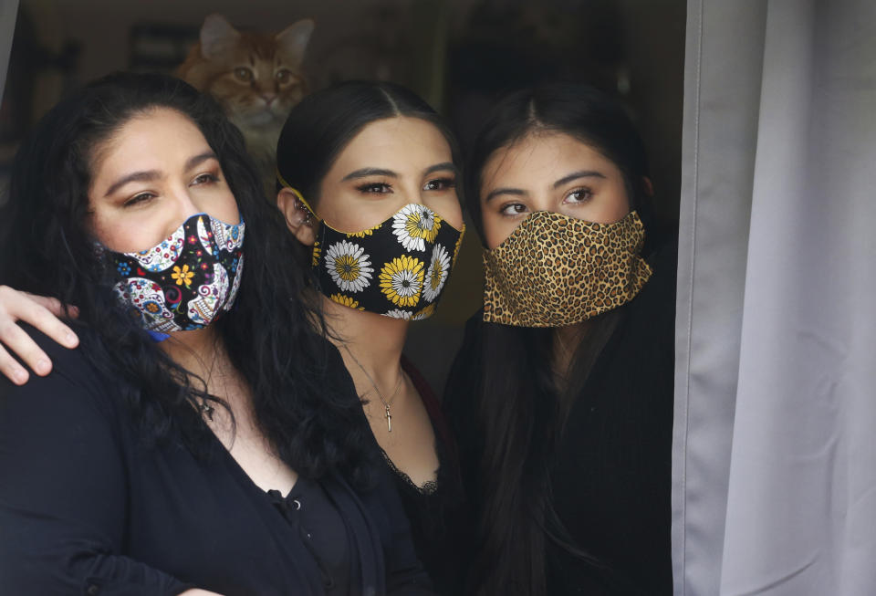 In this Monday, May 18, 2020, photo, Anissa Archuleta, center, sits at a window with her sister Alexis Archuleta, right, and her mother, Jaime Ortega, at their home in Midvale, Utah. Ortega and her two daughters had to get tested and be monitored for two weeks after they stopped by a birthday party for a young cousin whose father unknowingly had the coronavirus. The women all tested negative, but received daily calls from health investigator Maria DiCaro to check on their symptoms. (AP Photo/Rick Bowmer)