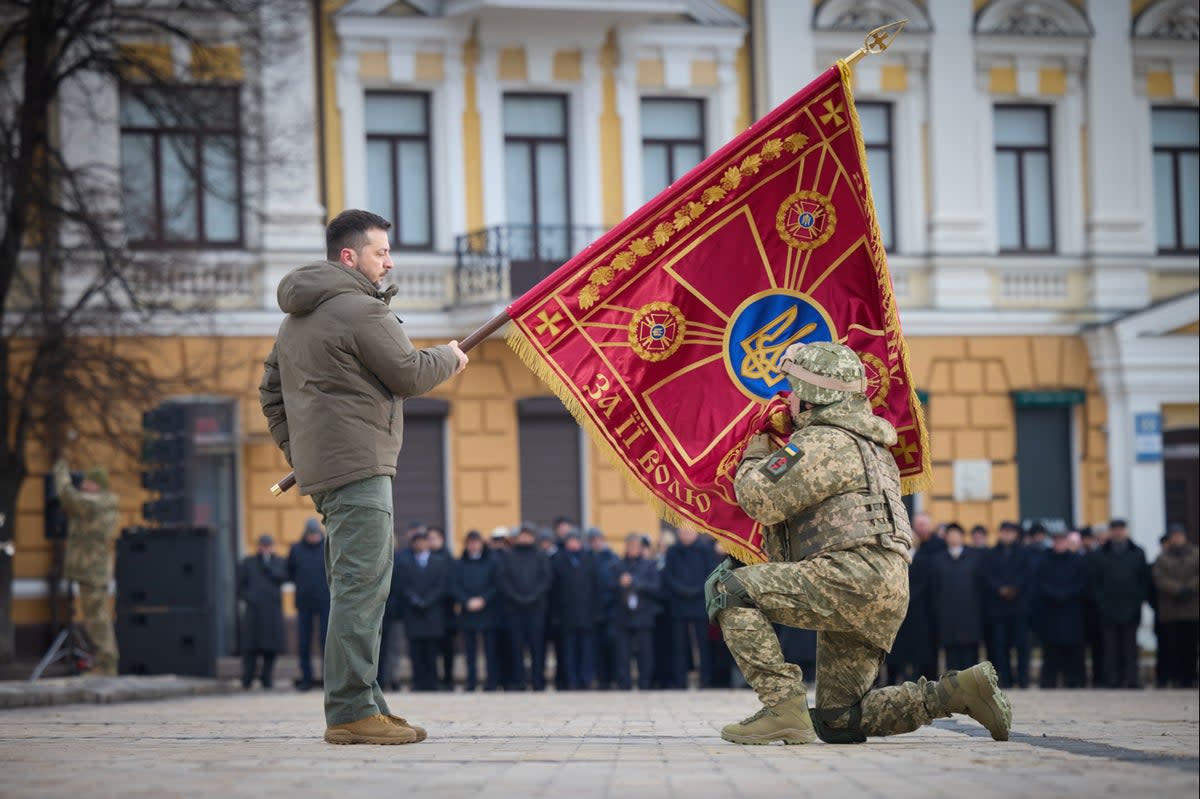 Ukrainian President Volodymyr Zelensky, left, holds the flag of a military unit as an officer kisses it, during commemorative event on the occasion of the Russia Ukraine war one year anniversary in Kyiv (AP)
