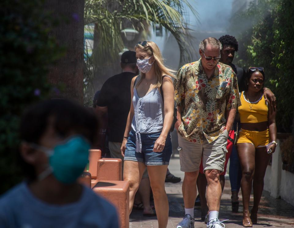 People with or without masks walk through downtown Palm Springs, Calif. , on Sunday.