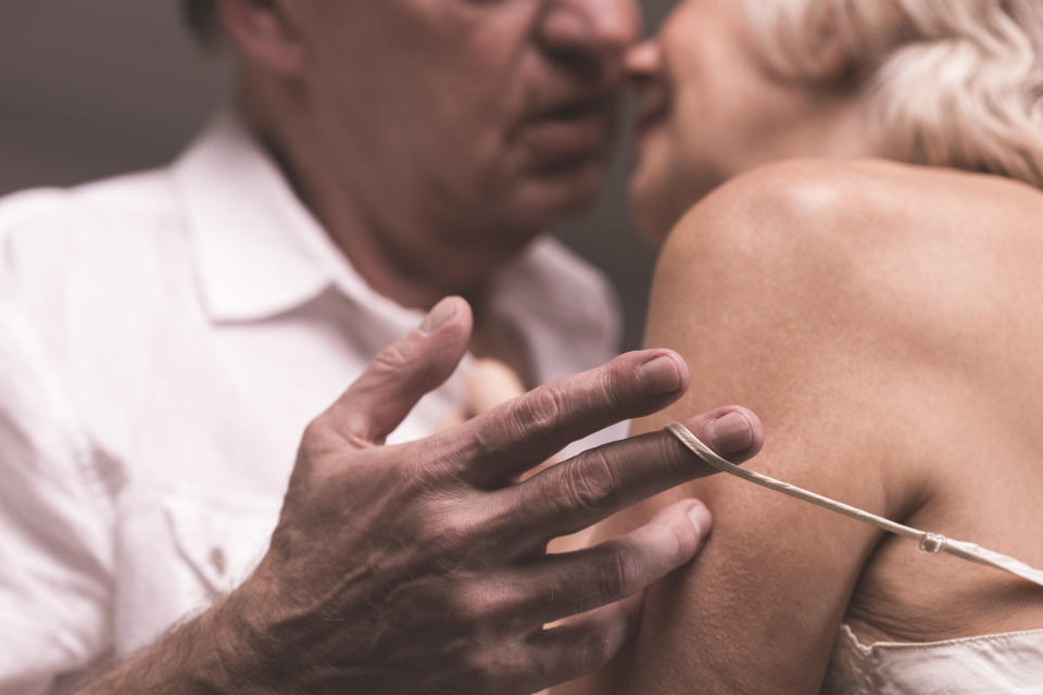 Elder couple bodies close to each other with the man's hand stripping shoulder-strap of woman's underwear