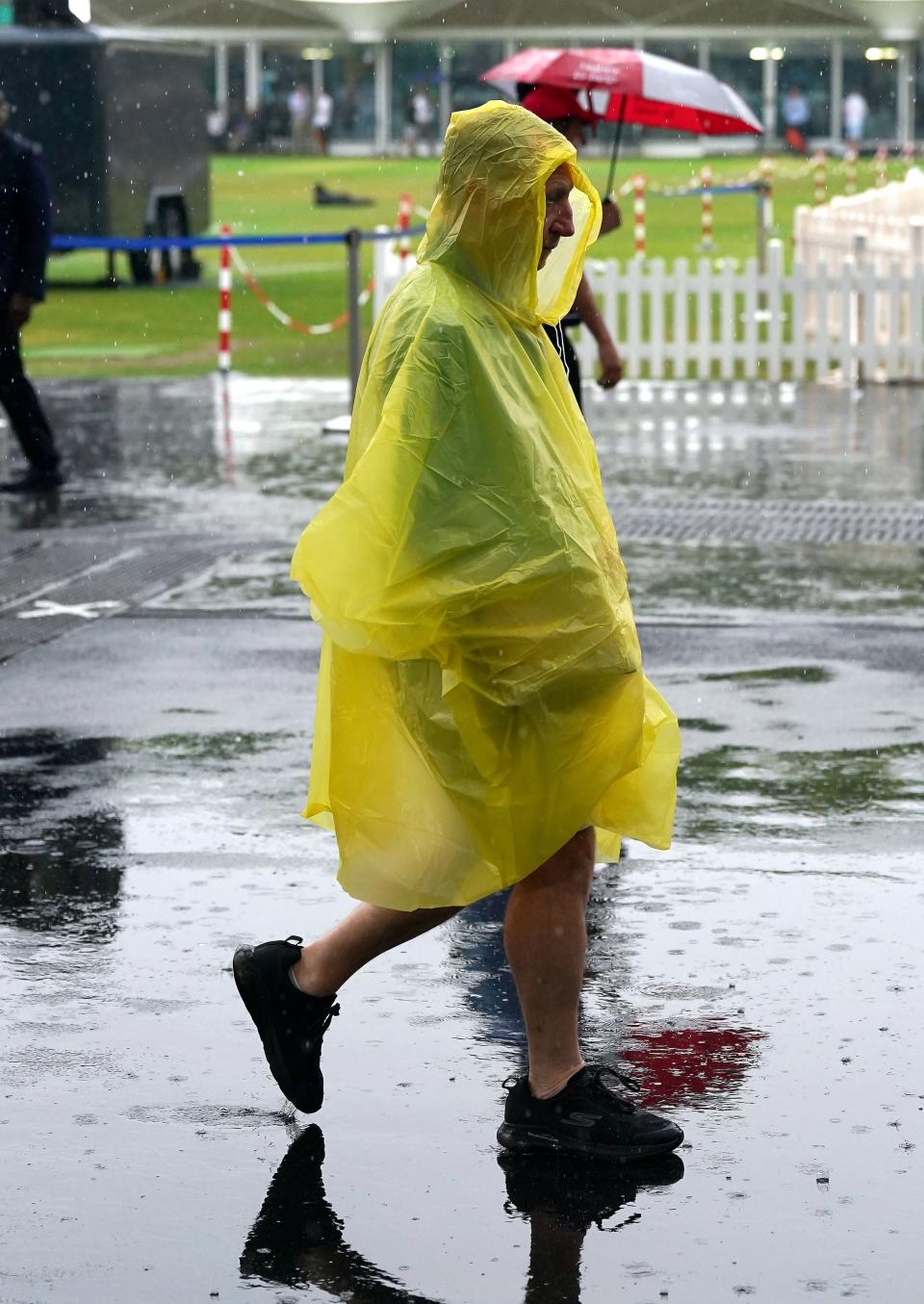 A spectator covers up in the rain (PA)