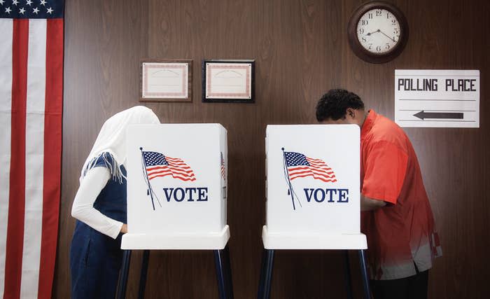 Two individuals at voting booths with "VOTE" banners, American flag in background, indicating a polling place