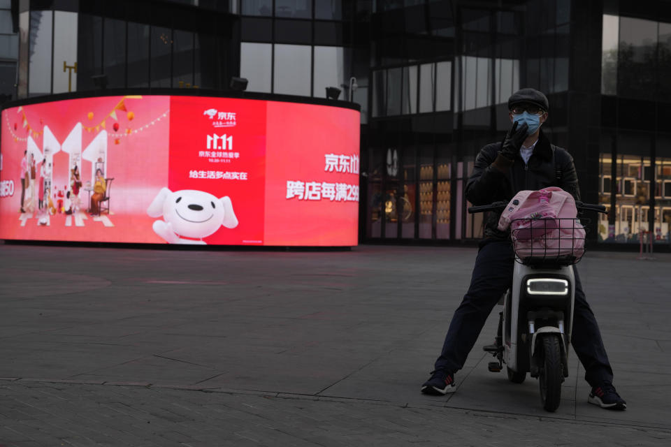 A man adjusts his mask as he waits near an ad from JD.com for Singles' Day in Beijing, Thursday, Nov. 10, 2022. China's biggest online shopping festival, Singles' Day, is muted this year with sales numbers expected to grow slowly amid an uncertain economy and COVID-19. Singles’ Day — also known as Double 11 as it falls on Nov. 11 annually — is closely watched as a barometer of consumption in China. (AP Photo/Ng Han Guan)
