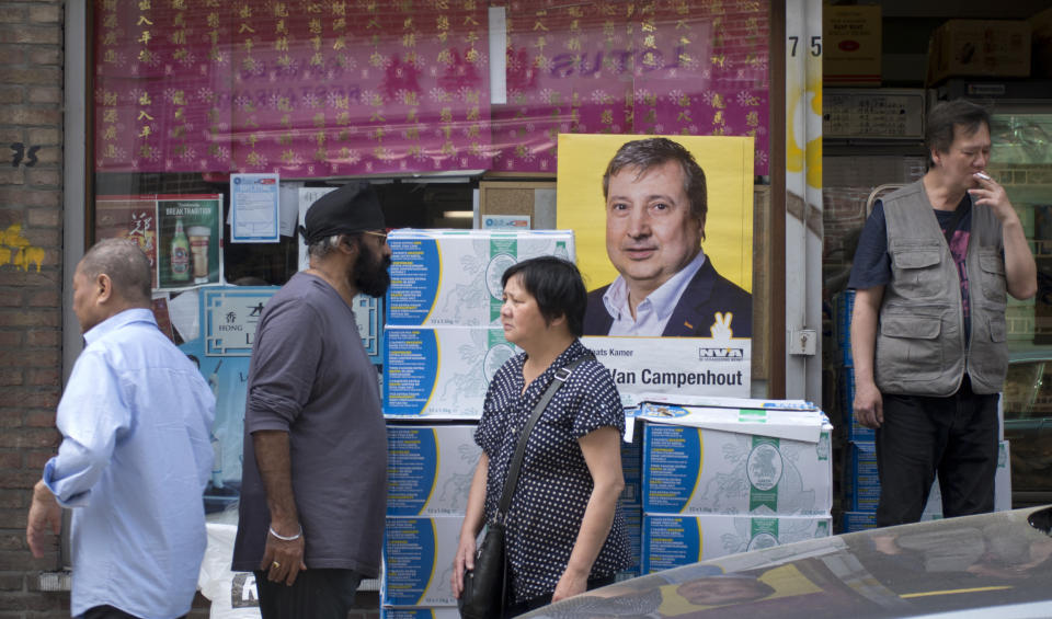 People walk by an election poster in the window of an Asian food store in the Chinatown quarter of Antwerp, Belgium, Thursday, May 23, 2019. Belgium, which has one of the oldest compulsory voting systems, will go to the polls for regional, federal and European elections on May 26, 2019. (AP Photo/Virginia Mayo)