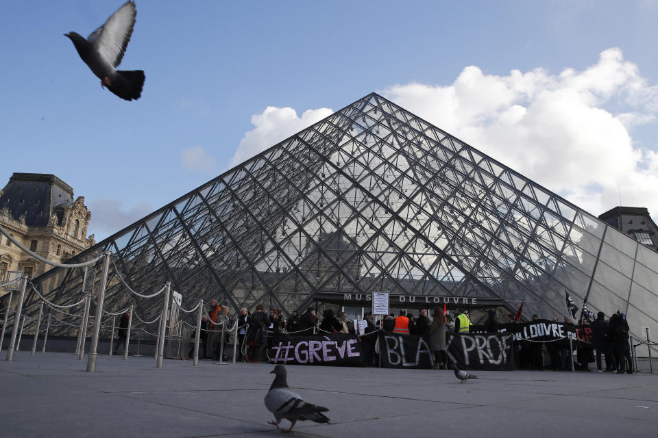 Pigeons fly by the Louvre pyramid as striking employees demonstrate outside the museum Friday, Jan. 17, 2020 in Paris. Paris' Louvre museum was closed Friday as dozens of protesters blocked the entrance to denounce the French government's plans to overhaul the pension system. (AP Photo/Francois Mori)