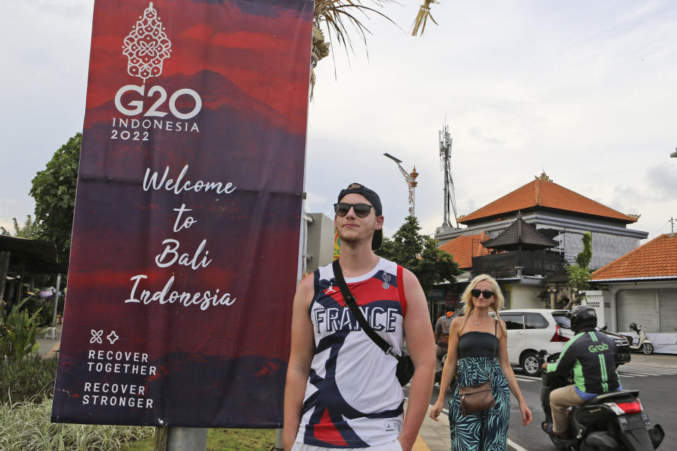 Tourists walk past a G20 banner in Nusa Dua, Bali, Indonesia on Friday, Nov. 11, 2022. The dozens of world leaders and other dignitaries traveling to Bali for the G-20 summit will be drawing a welcome spotlight on the revival of the tropical island's ailing tourism sector after a two-year closure to foreign travelers due to the pandemic. (AP Photo/Firdia Lisnawati)