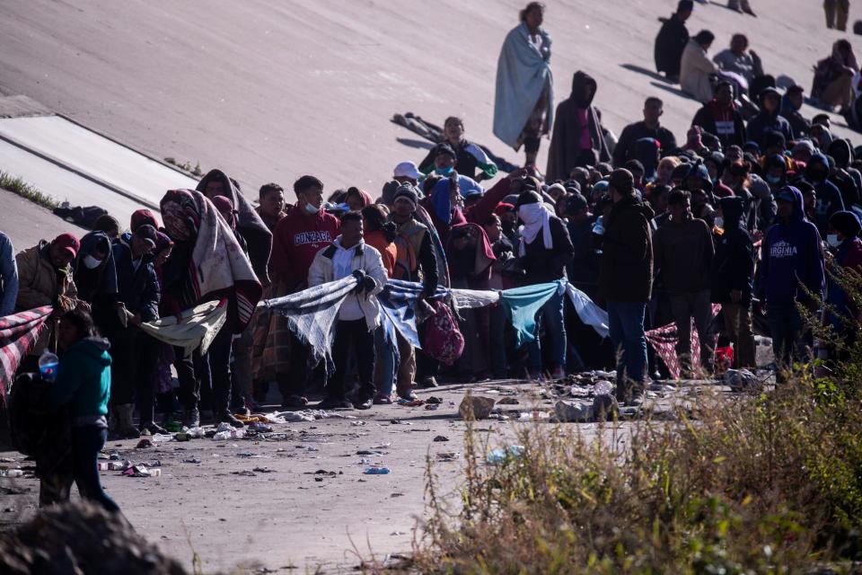 Migrants tie blankets together as a rope to prevent other migrants from jumping the line as they are processed by Customs and Border Protection in El Paso, Texas. The migrants had spent the night in the north embankment of the Rio Grande after crossing en mass on Sunday, Dec. 11, 2022. 